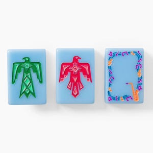 Puede incluir: Tres fichas rectangulares de color azul claro con dise&ntilde;os grabados. La primera muestra un p&aacute;jaro del trueno verde, la segunda un p&aacute;jaro del trueno rojo y la tercera un borde de notas musicales coloridas alrededor de un saxof&oacute;n naranja.