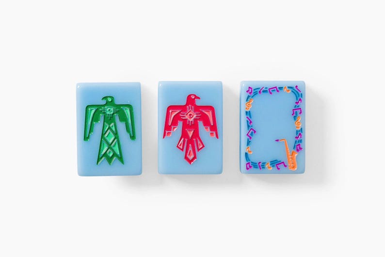 Puede incluir: Tres fichas rectangulares de color azul claro con dise&ntilde;os grabados. La primera muestra un p&aacute;jaro del trueno verde, la segunda un p&aacute;jaro del trueno rojo y la tercera un borde de notas musicales coloridas alrededor de un saxof&oacute;n naranja.