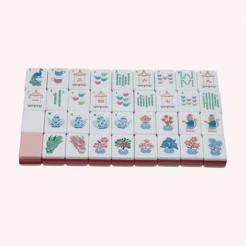 May include: A set of white rectangular mahjong tiles arranged in a grid, featuring colorful illustrations of teapots, teacups, bamboo stalks, flowers, dragons, and Chinese characters. One tile is solid pink, and two tiles are labeled as Joker.