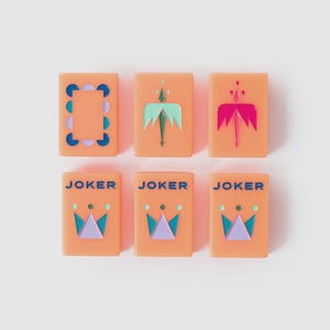 May include: Six rectangular peach-colored tiles arranged in two rows. The top row features a patterned border tile, a light green arrow design, and a dark pink arrow design. The bottom row contains three identical tiles labeled JOKER in blue text above a crown graphic in light green, dark blue, and light purple.
