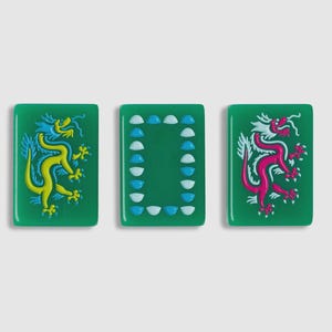 May include: Three rectangular green mahjong tiles. The left tile features a yellow dragon, the right tile features a pink dragon, and the center tile displays a rectangular border composed of small, alternating light blue and white semi-circles.