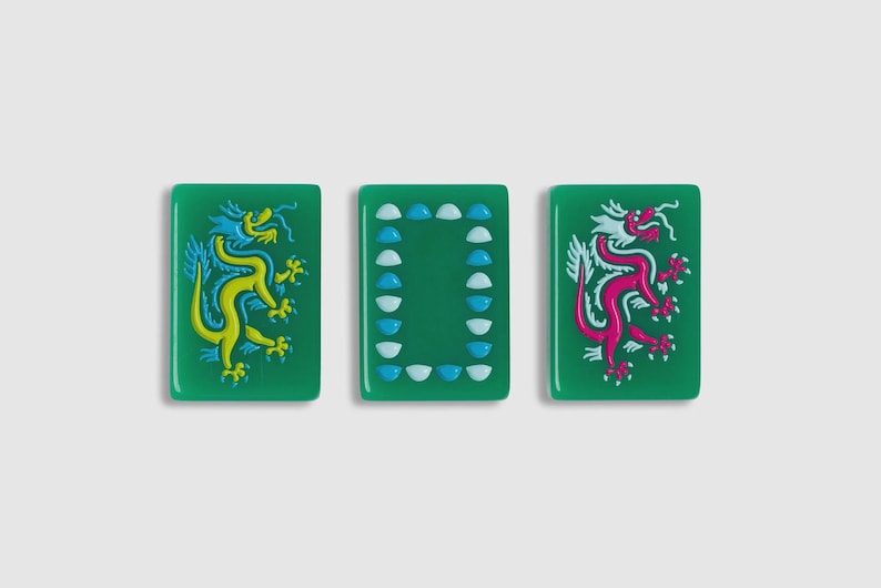 May include: Three rectangular green mahjong tiles. The left tile features a yellow dragon, the right tile features a pink dragon, and the center tile displays a rectangular border composed of small, alternating light blue and white semi-circles.