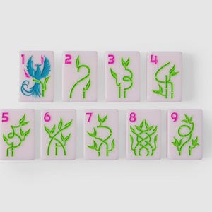Puede incluir: Un conjunto de nueve fichas de mahjong rectangulares con una base de color lavanda claro. Cada ficha presenta un n&uacute;mero rosa brillante del uno al nueve en la esquina superior izquierda y un dise&ntilde;o gr&aacute;fico de bamb&uacute; verde, con un f&eacute;nix azul en el uno.