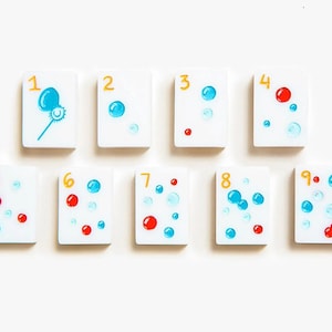 May include: A set of nine rectangular white tiles arranged in two rows, each featuring a yellow numeral from one to nine and a corresponding number of blue and red circular bubble illustrations, with the first tile showing a bubble wand.