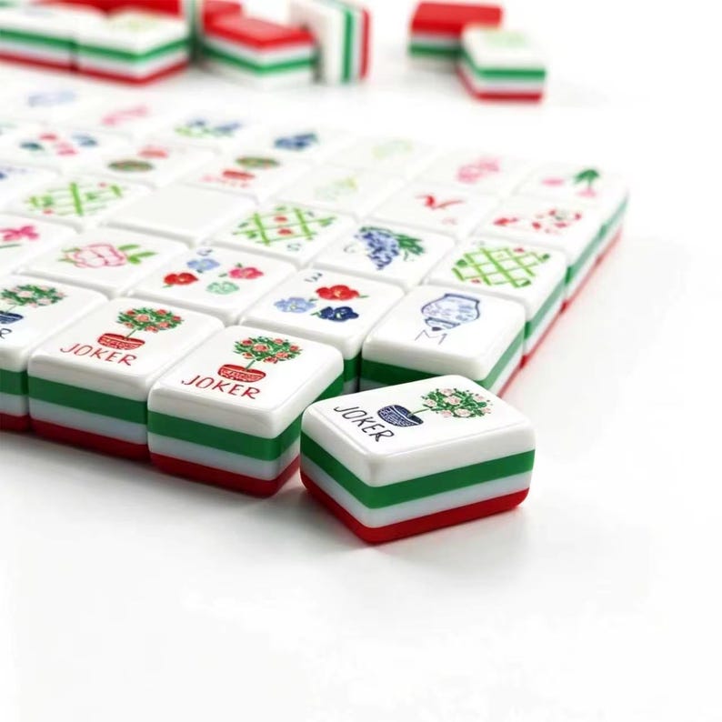 May include: A set of rectangular mahjong tiles with white tops and layered green and red bases. The tiles feature colorful illustrations of potted plants, flowers, and patterns. Several tiles are labeled with the word JOKER in red text.