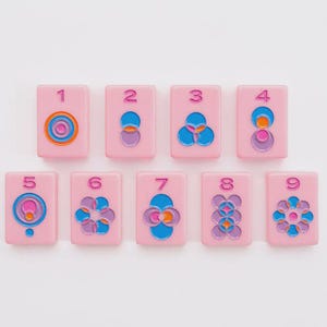 May include: A set of nine rectangular pink tiles, each featuring a unique geometric pattern in blue, purple, and orange, with a corresponding number from one to nine embossed in pink at the top of each tile. The tiles are arranged in two rows.