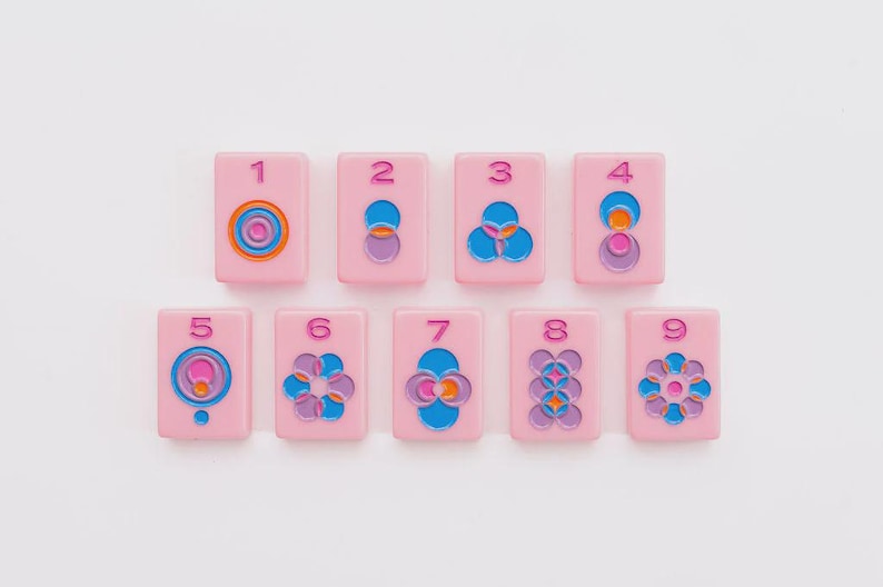 May include: A set of nine rectangular pink tiles, each featuring a unique geometric pattern in blue, purple, and orange, with a corresponding number from one to nine embossed in pink at the top of each tile. The tiles are arranged in two rows.