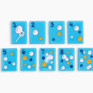 May include: A set of nine rectangular light blue tiles, each featuring a dark blue numeral from one to nine. The tiles are decorated with various small circles in white, yellow, and dark blue, with the number one tile showing a bubble wand.