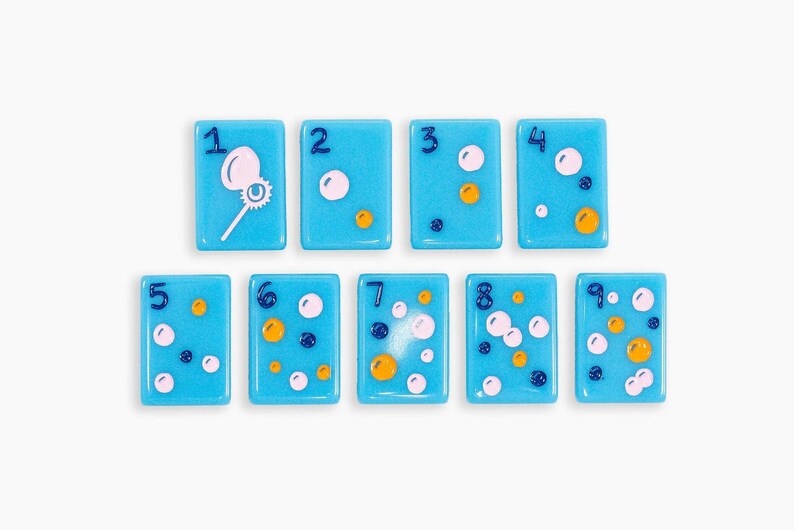 May include: A set of nine rectangular light blue tiles, each featuring a dark blue numeral from one to nine. The tiles are decorated with various small circles in white, yellow, and dark blue, with the number one tile showing a bubble wand.