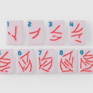 Puede incluir: Un conjunto de nueve fichas de mahjong rectangulares de color rosa claro dispuestas en dos filas. Cada ficha presenta un n&uacute;mero azul del uno al nueve en la esquina superior izquierda y una cantidad correspondiente de s&iacute;mbolos rojos grabados.
