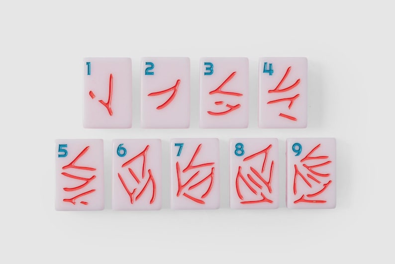 Puede incluir: Un conjunto de nueve fichas de mahjong rectangulares de color rosa claro dispuestas en dos filas. Cada ficha presenta un n&uacute;mero azul del uno al nueve en la esquina superior izquierda y una cantidad correspondiente de s&iacute;mbolos rojos grabados.