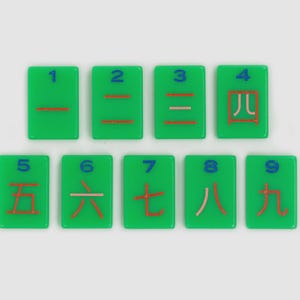 May include: Nine rectangular green tiles arranged in two rows. Each tile features a blue Arabic numeral from 1 to 9 at the top and a corresponding red Chinese character for that number below it. The tiles have a smooth, glossy finish.
