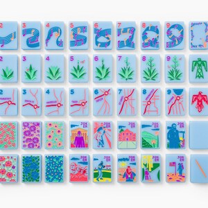 Puede incluir: Un conjunto de fichas de mahjong rectangulares de color azul claro con dise&ntilde;os impresos coloridos que incluyen notas musicales, plantas del desierto, mapas de ciudades, patrones florales y escenas ilustradas marcadas como Joker y N, E, W, S.