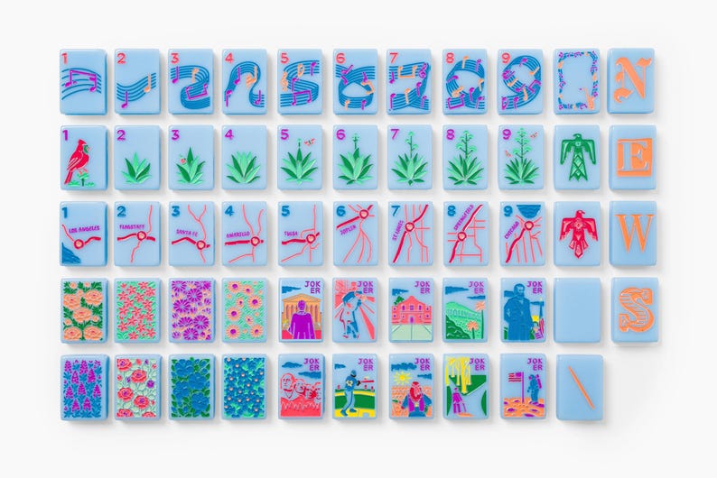 Puede incluir: Un conjunto de fichas de mahjong rectangulares de color azul claro con dise&ntilde;os impresos coloridos que incluyen notas musicales, plantas del desierto, mapas de ciudades, patrones florales y escenas ilustradas marcadas como Joker y N, E, W, S.