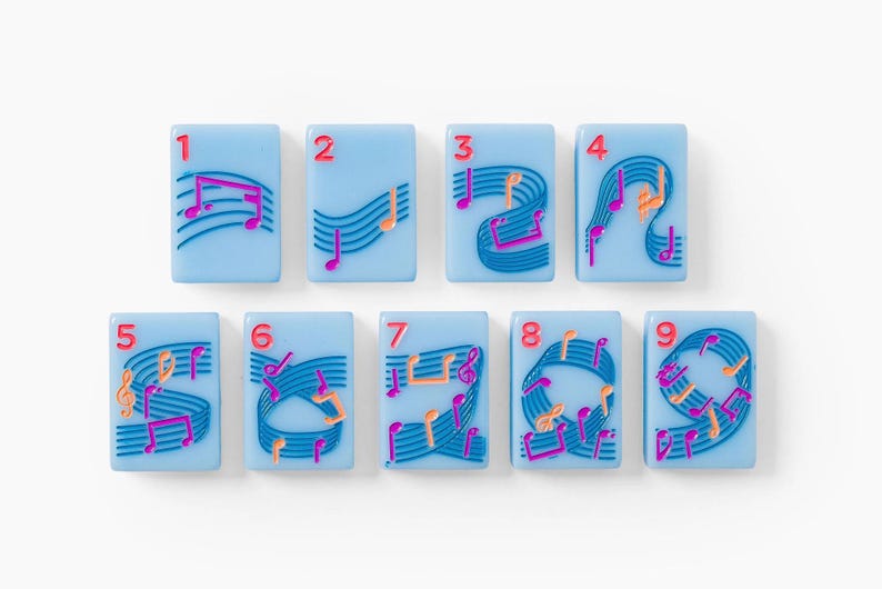 Puede incluir: Un conjunto de nueve fichas rectangulares de color azul claro, cada una con un n&uacute;mero rojo del uno al nueve en la esquina superior izquierda. Las fichas est&aacute;n decoradas con pentagramas azul oscuro y notas musicales rosas y naranjas.