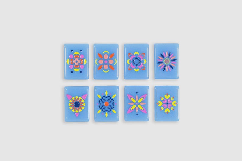 May include: Eight rectangular light blue glass tiles arranged in two rows of four. Each tile features a unique, symmetrical floral or geometric pattern painted in vibrant colors including pink, yellow, orange, and dark blue, creating a set.