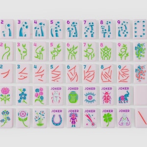 Puede incluir: Un conjunto de fichas de mahjong rectangulares con base de color rosa claro. Las fichas presentan dise&ntilde;os grabados coloridos que incluyen los n&uacute;meros del uno al nueve, marcadores direccionales North, East, South, West e iconos florales, animales y joker.