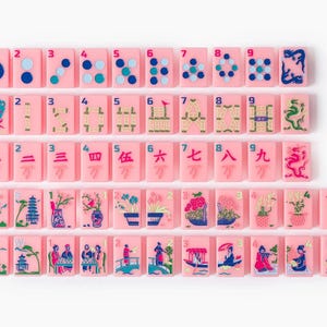 Puede incluir: Un conjunto de fichas de mahjong rectangulares de color rosa dispuestas en cinco filas. Las fichas presentan varias ilustraciones coloridas que incluyen n&uacute;meros, caracteres chinos, dragones, flores y escenas tradicionales. Una ficha tiene el texto BIG JOKER.