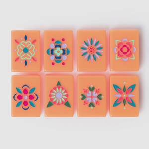 May include: Eight rectangular peach-colored tiles arranged in two rows of four. Each tile features a unique, symmetrical floral or geometric pattern painted in vibrant shades of teal, magenta, lavender, and dark blue, creating a colorful set.