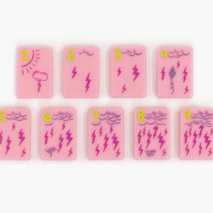 May include: Nine rectangular pink tiles arranged in two rows. Each tile features a lime green number from one to nine and purple line art illustrations of weather patterns, including clouds, sun, lightning bolts, a kite, and a paper airplane.