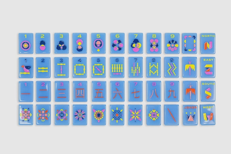 May include: A set of rectangular light blue tiles arranged in a grid, featuring colorful graphic designs, numbers one through nine, and directional labels including North, East, South, and West in yellow, pink, and dark blue ink.