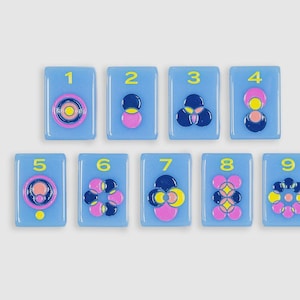 May include: Nine rectangular light blue tiles arranged in two rows, each featuring a yellow number from one to nine and a unique raised geometric pattern composed of pink, dark blue, and yellow circular shapes in a glossy, smooth finish.