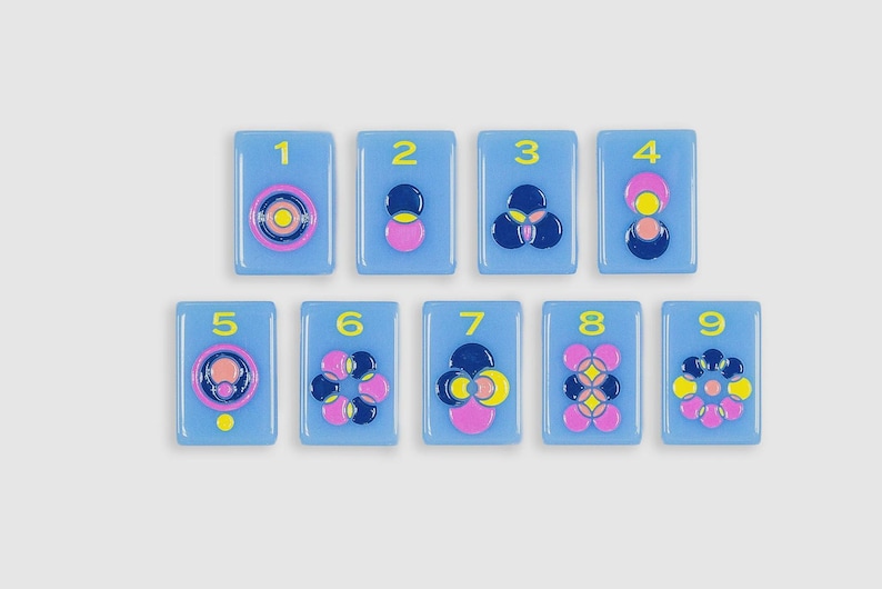 May include: Nine rectangular light blue tiles arranged in two rows, each featuring a yellow number from one to nine and a unique raised geometric pattern composed of pink, dark blue, and yellow circular shapes in a glossy, smooth finish.