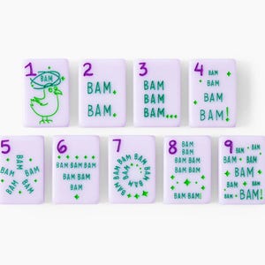 Pu&ograve; includere: Un set di nove tessere rettangolari color viola chiaro disposte su due file. Ogni tessera presenta un numero viola da uno a nove e testo verde con la scritta BAM in varie disposizioni, inclusa un'illustrazione di un uccello.