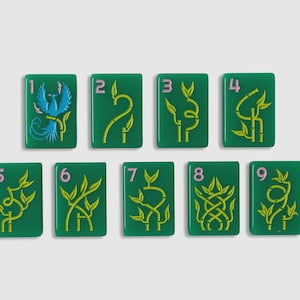 May include: A set of nine rectangular green mahjong tiles arranged in two rows. Each tile features a light pink numeral from one to nine and a yellow bamboo-style graphic, except for the number one tile, which displays a blue phoenix illustration.