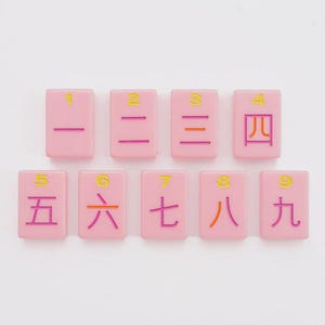 May include: A set of nine rectangular pink tiles arranged in two rows. Each tile features a yellow Arabic numeral from one to nine at the top and a corresponding Chinese character in purple or orange ink centered below the number on the tile surface.