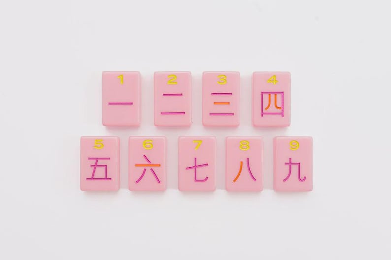 May include: A set of nine rectangular pink tiles arranged in two rows. Each tile features a yellow Arabic numeral from one to nine at the top and a corresponding Chinese character in purple or orange ink centered below the number on the tile surface.