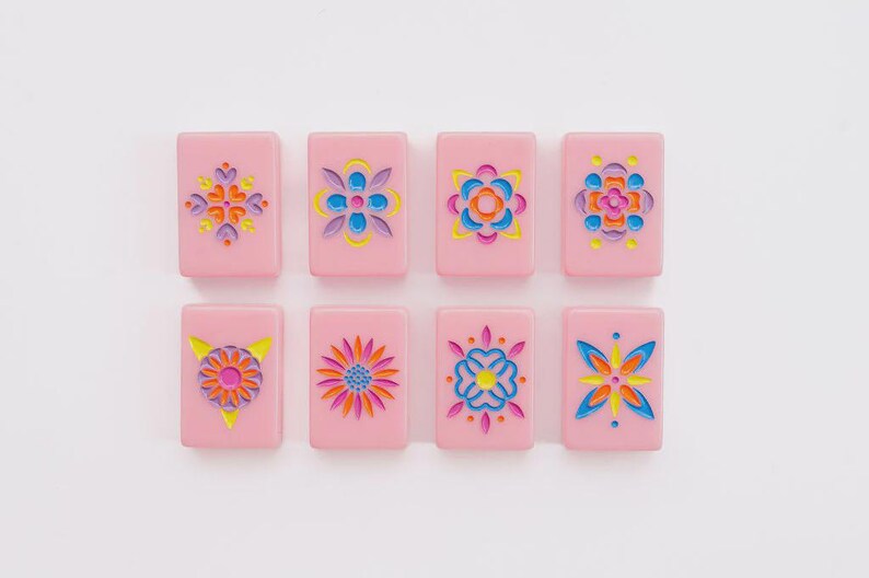 May include: Eight rectangular pink tiles arranged in two rows of four. Each tile features a unique, recessed floral or geometric pattern engraved into the surface, filled with vibrant colors including yellow, blue, orange, and magenta.