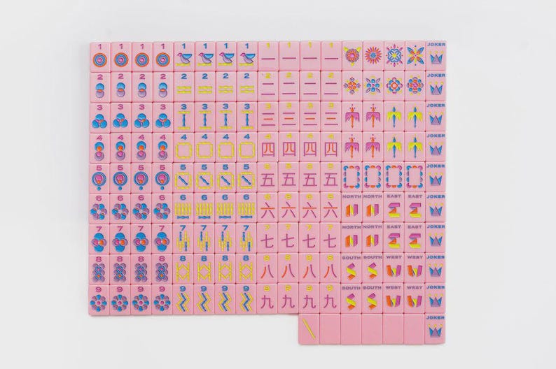 May include: A set of pink Mahjong tiles arranged in a grid, featuring colorful engraved numbers, symbols, and characters in blue, yellow, and red. The tiles include numbered suits, directional markers, floral patterns, and Joker tiles with crown icons.