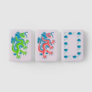 Puede incluir: Tres fichas de mahjong rectangulares con una base de color rosa p&aacute;lido. Dos fichas presentan una ilustraci&oacute;n detallada de un drag&oacute;n, una en verde vibrante y la otra en rojo brillante. La tercera ficha muestra un borde rectangular de semic&iacute;rculos azules.
