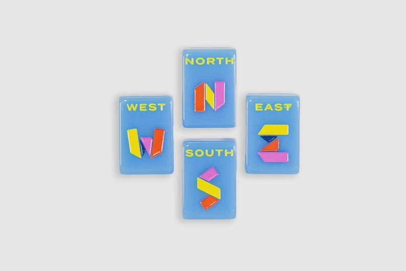 May include: Four rectangular light blue tiles arranged in a cross shape. Each tile features a yellow compass direction label: NORTH, SOUTH, EAST, and WEST. Below each label is a stylized letter N, S, E, or W constructed from colorful geometric shapes.