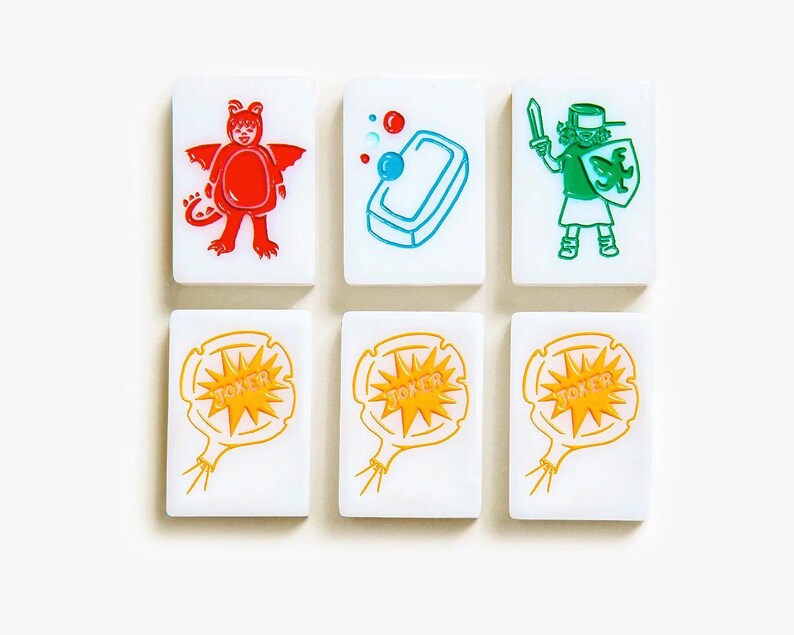 May include: Six white rectangular mahjong tiles arranged in two rows. The top row features a red dragon costume, a blue bar of soap with bubbles, and a green knight with a sword and shield. The bottom row shows three identical yellow joker balloons.
