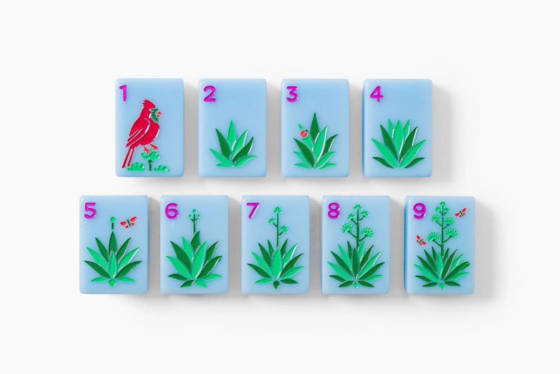 Puede incluir: Un conjunto de nueve fichas de mahjong rectangulares de color azul claro dispuestas en dos filas. Cada ficha presenta un n&uacute;mero magenta del uno al nueve y una ilustraci&oacute;n de una planta de agave verde. La primera incluye un cardenal rojo.