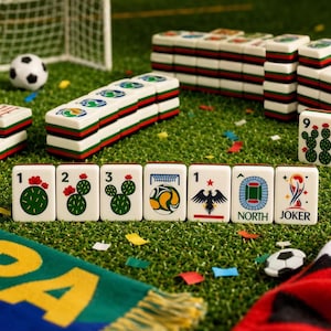May include: A set of white mahjong tiles featuring green cactus illustrations, soccer balls, a stadium, an eagle, and a Joker tile. The tiles are arranged on a green surface with a small soccer ball and a goal net visible in the background.