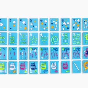 May include: A collection of forty-four rectangular light blue tiles arranged in four rows. Each tile features colourful illustrations, numbers, or letters. The designs include bubbles, lightning bolts, cans labelled flour, and various cartoon characters.
