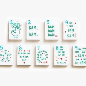 May include: A set of nine rectangular white tiles numbered one through nine in blue. Each tile features the word BAM in green text, repeated according to the number, with red accents including dots, diamonds, and a bird illustration on the one tile.