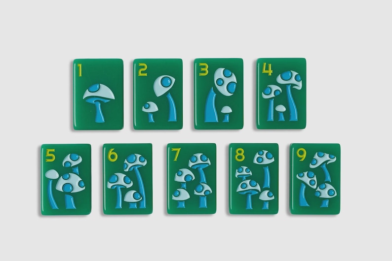 May include: A set of nine rectangular green tiles, each featuring a yellow number from one to nine and a raised blue and light blue mushroom design. The number of mushrooms on each tile corresponds to the numerical value displayed on the tile.