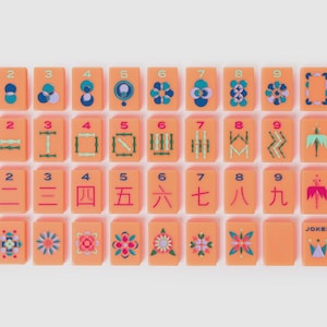 May include: A set of rectangular peach-colored mahjong tiles arranged in four rows. The tiles feature colorful geometric patterns, numbers one through nine, Chinese characters, directional labels, and a joker tile with a crown graphic design.