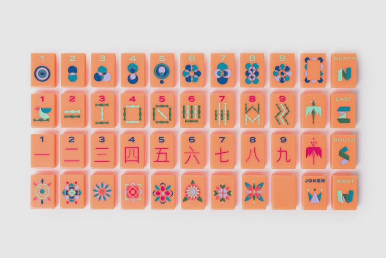 May include: A set of rectangular peach-colored mahjong tiles arranged in four rows. The tiles feature colorful geometric patterns, numbers one through nine, Chinese characters, directional labels, and a joker tile with a crown graphic design.