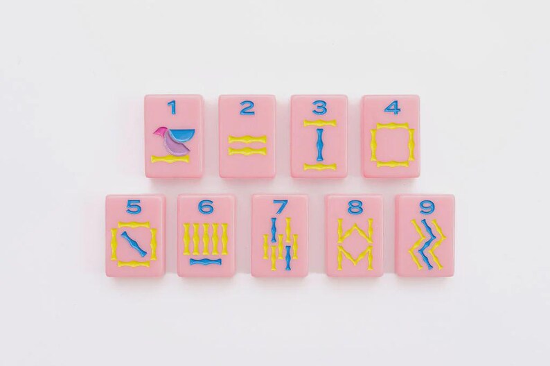 May include: A set of nine rectangular pink tiles arranged in two rows, each featuring a blue numeral from one to nine at the top. The tiles display various engraved patterns in yellow and blue, including geometric shapes, lines, and a bird icon.