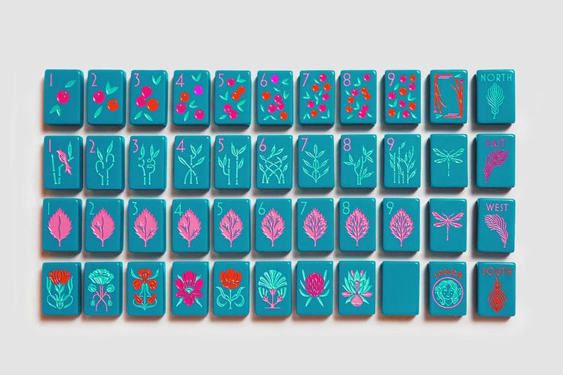 K&ouml;nnte beinhalten: Ein Set aus rechteckigen, blaugr&uuml;nen Mahjong-Spielsteinen, die in einem Raster angeordnet sind. Die Steine zeigen bunte Illustrationen von Beeren, Bambus, Bl&auml;ttern, Blumen, Libellen sowie Text wie North, East, West, South und ein Gesichtssymbol.