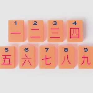 May include: A set of nine rectangular peach-colored tiles arranged in two rows. Each tile features a blue Arabic numeral from 1 to 9 at the top and a corresponding red Chinese character representing the same number centered below the numeral.