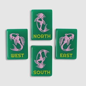 May include: Four rectangular green mahjong tiles featuring a light pink koi fish illustration and the yellow text NORTH, SOUTH, EAST, and WEST. Each tile displays a stylized fish design oriented differently, with the cardinal direction printed below.
