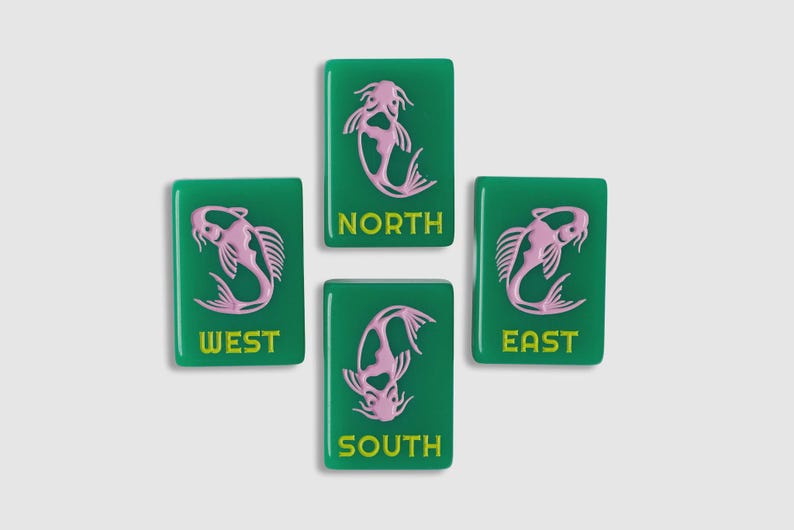 May include: Four rectangular green mahjong tiles featuring a light pink koi fish illustration and the yellow text NORTH, SOUTH, EAST, and WEST. Each tile displays a stylized fish design oriented differently, with the cardinal direction printed below.