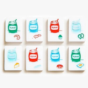 May include: Eight rectangular white tiles featuring colorful illustrations of flour sacks and various baked goods. Each tile displays a sack labeled "FLOUR" in red, green, or blue, accompanied by icons of a croissant, cookies, muffin, pretzel, cheese, bread, donut, or toast.