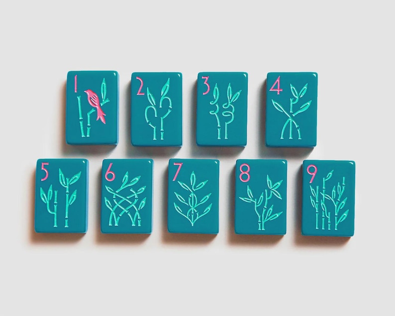K&ouml;nnte beinhalten: Neun rechteckige, blaugr&uuml;ne Mahjong-Spielsteine in zwei Reihen. Jeder Stein zeigt eine pinkfarbene Ziffer von eins bis neun in der oberen linken Ecke und eine hellgr&uuml;ne Bambus-Illustration. Der erste Stein enth&auml;lt einen pinkfarbenen Vogel.